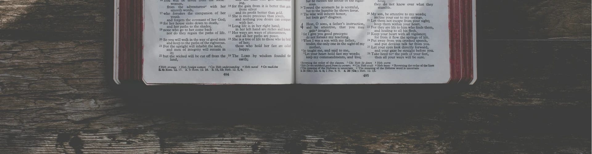 A Bible with red edging sitting on top of a rough wooden surface.