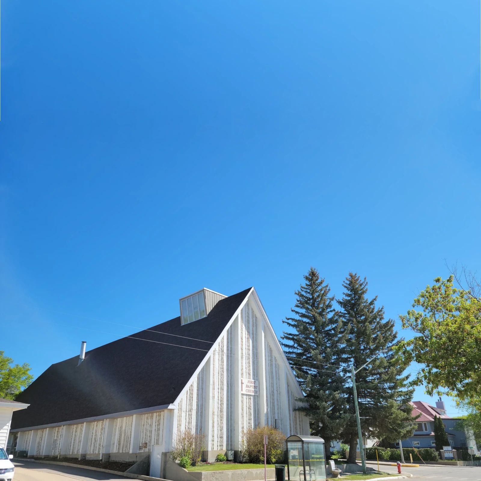 White A-frame baptist church building with black roof set under a clear blue sky.