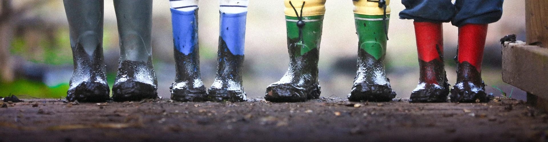 4 Kids wearing muddy boots that are varying birght colours.