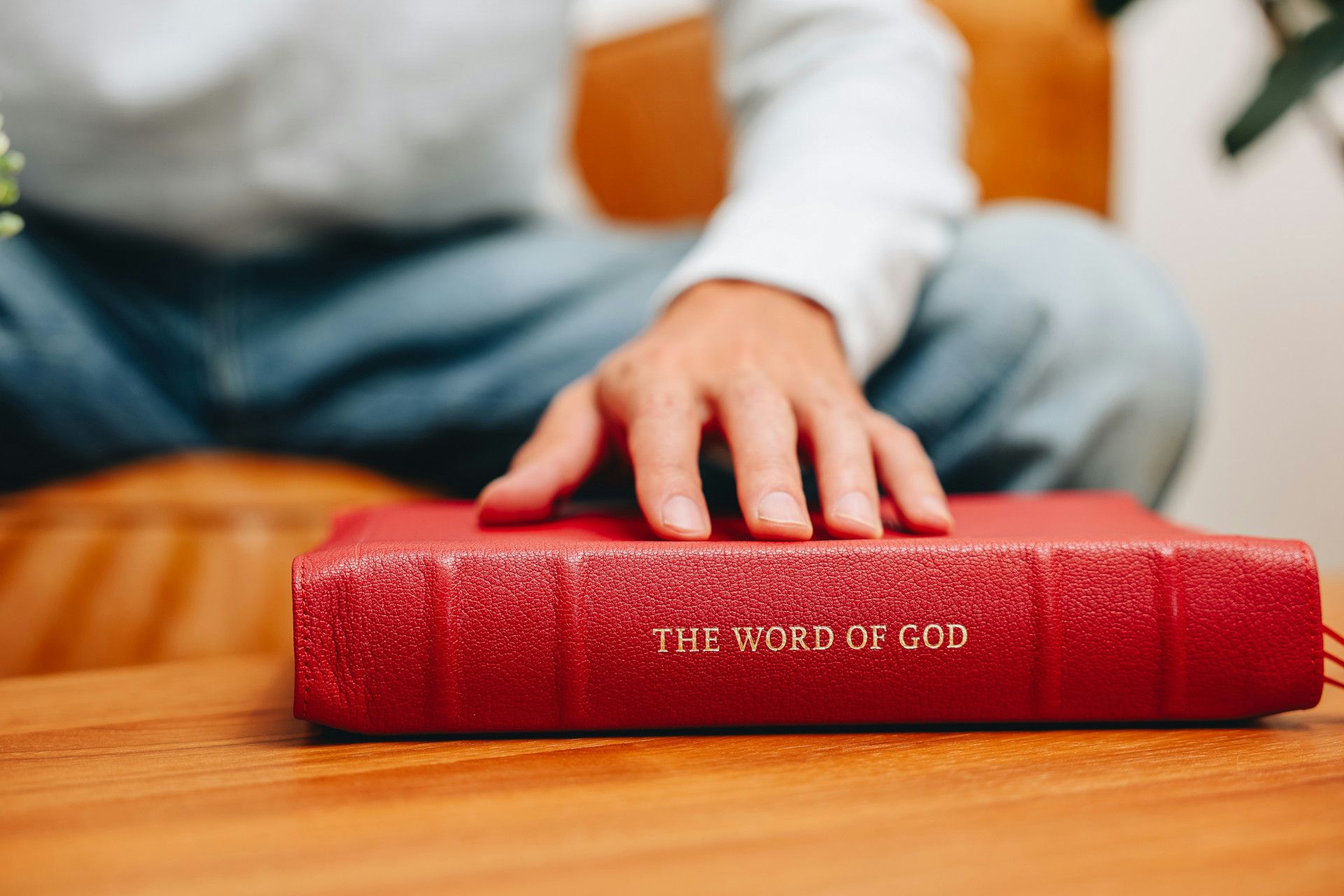 A man sitting on with his hand on a Red bible that reads "The Word of God".